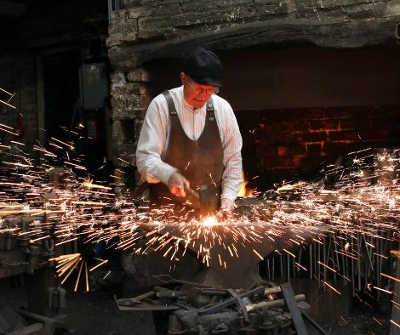 Blacksmith hitting a piece of metal with sparks flying across a workshop.