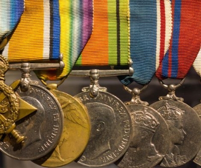 Close up of a mixture of silver and gold war medals all with multicoloured straps.