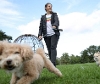 Owner walking their dog in the park on a lead with a little dog behind them. 