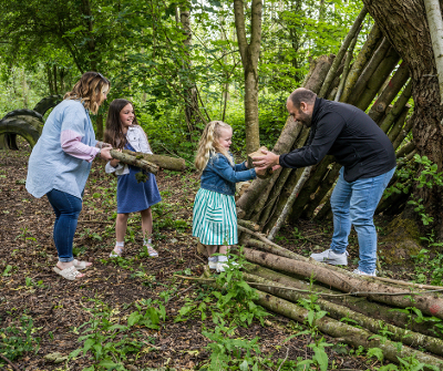 Family creating small wooden shelter in park woods.