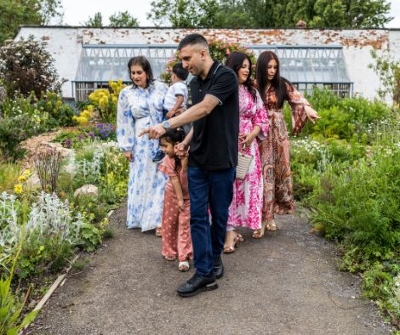 Group of people ranging from adults to young children walking on a gravel path pointing at the different coloured flowers around them