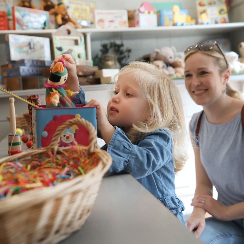 Little Girl With Mum Playing With Traditional Toys In The Toy Shop An image of a little Girl playing with traditional toys
