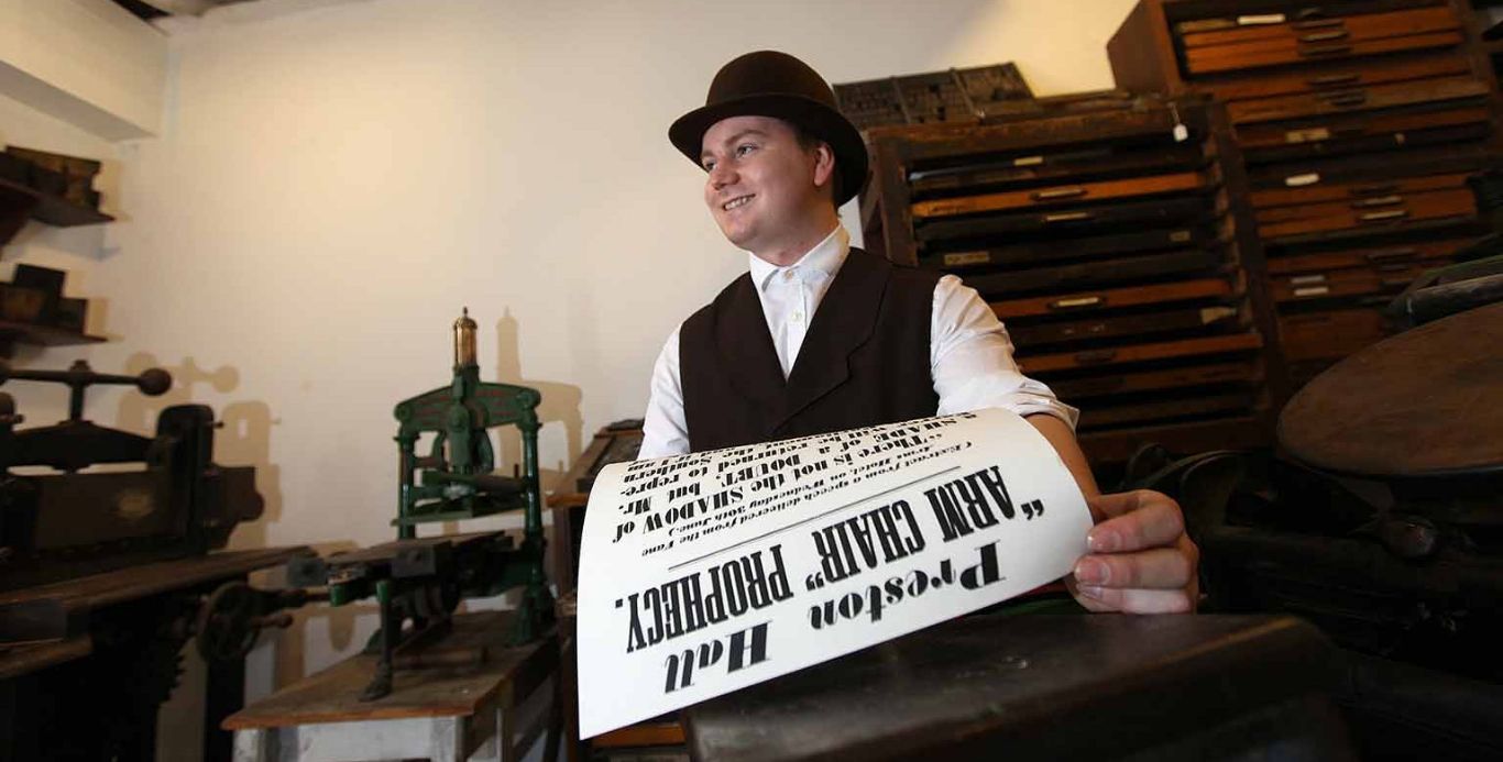 News Preston Park An image of a costumed interpreter holding a newspaper in the printers on the Victorian Street